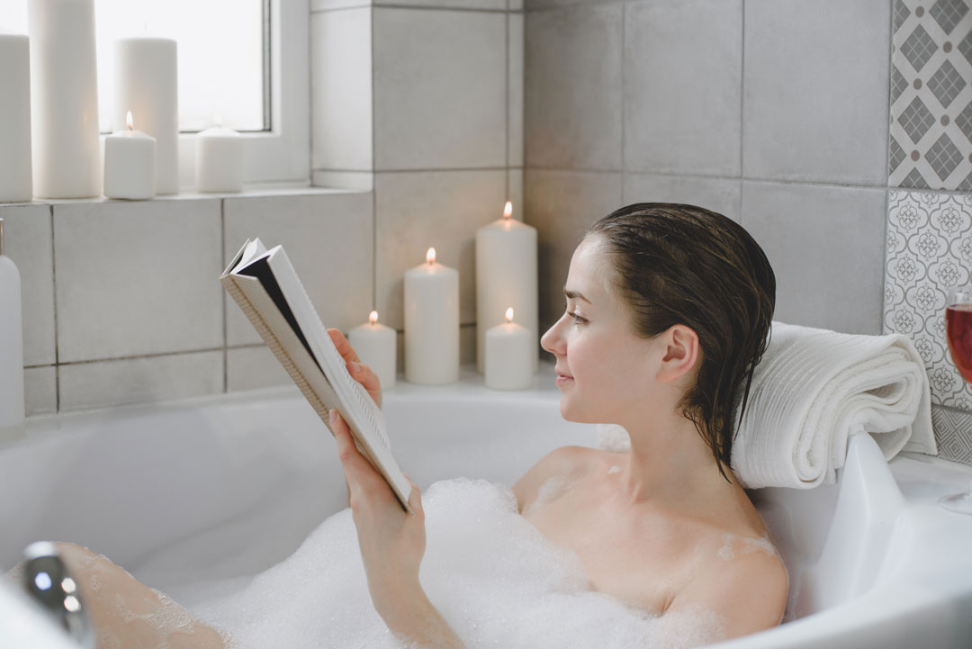 woman relaxing in a bubble bath with candles reading